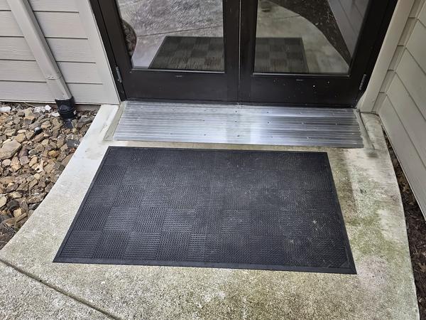 New aluminum ramp threshold set in concrete at a pair of dark entrance doors, with a mat in front