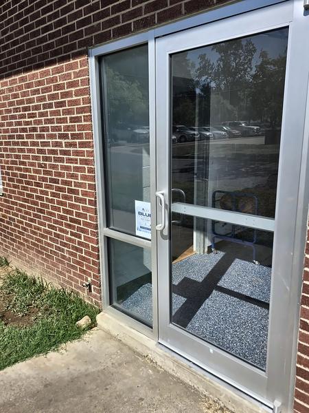 Single clear-anodized aluminum storefront entry door with glass on a red brick building
