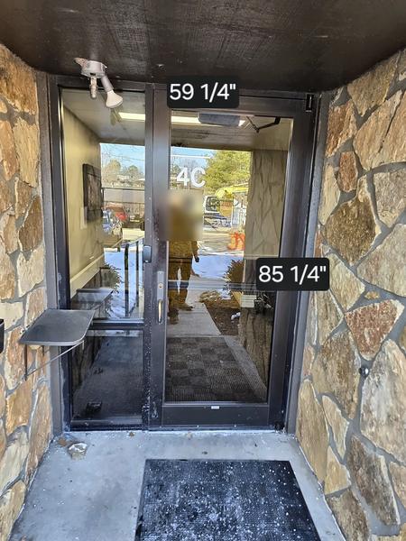 Narrow dark aluminum entrance door set between stone walls, with on-site measurement labels of 59 1/4 inches and 85 1/4 inches