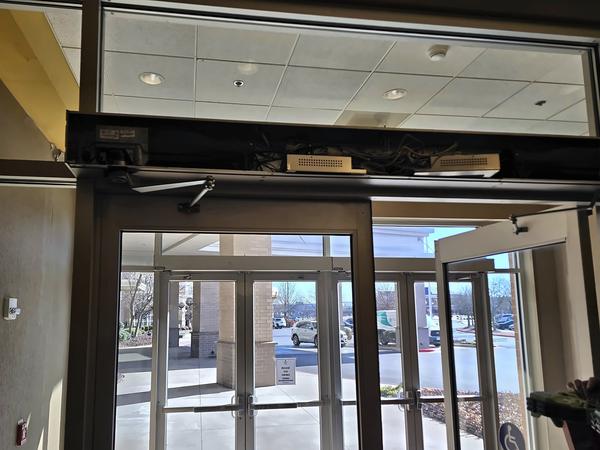 Automatic door operator header above an aluminum-framed glass entrance, viewed from inside the vestibule