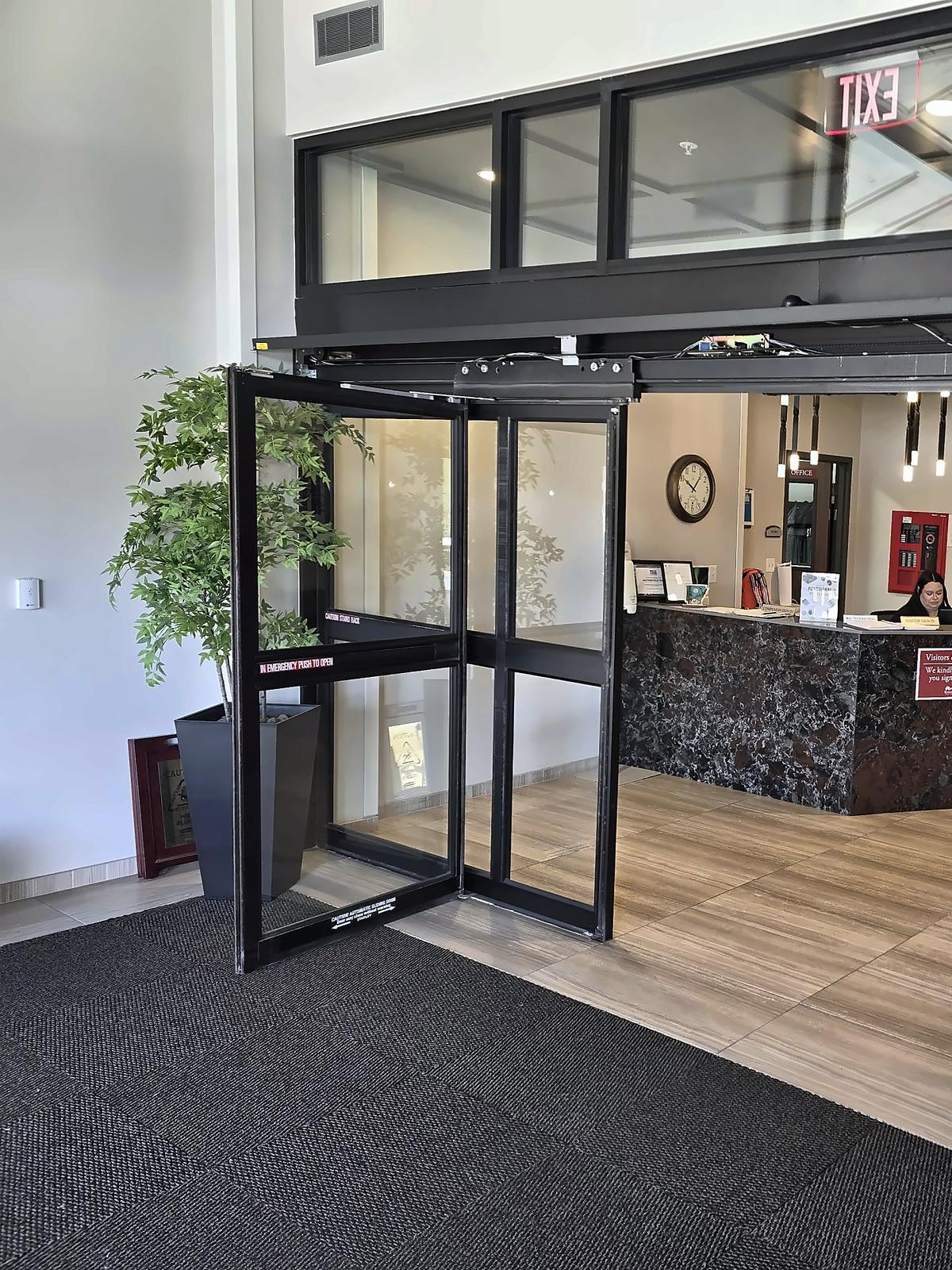 Open automatic aluminum-and-glass entrance doors with an overhead transom, leading into a lobby