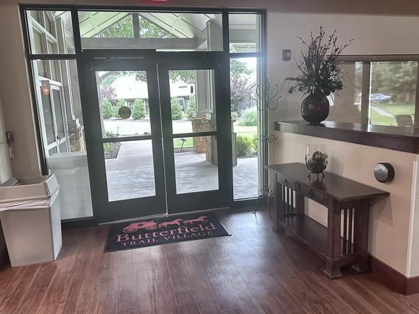 Interior view of a dark-framed double glass entrance with sidelites and transom, a welcome mat and a side table