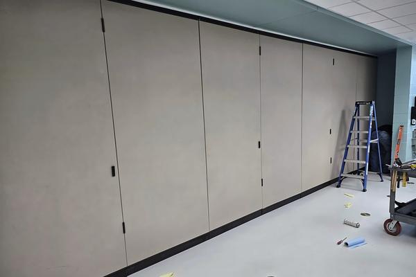 Large beige folding partition wall closed across a room, with a service cart and ladder nearby